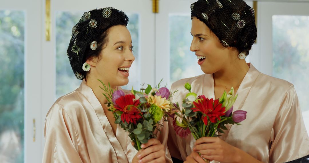 Two Women with Hair Rollers Holding Flowers Laughing Together - Free Images, Stock Photos and Pictures on Pikwizard.com