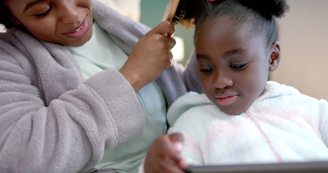 Mother Brushing Daughter's Hair While She Looks at Tablet - Free Images, Stock Photos and Pictures on Pikwizard.com