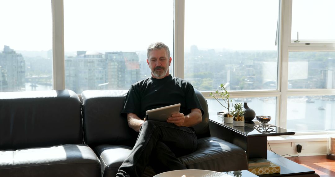 Middle-aged man relaxing with tablet in modern home living room - Free Images, Stock Photos and Pictures on Pikwizard.com