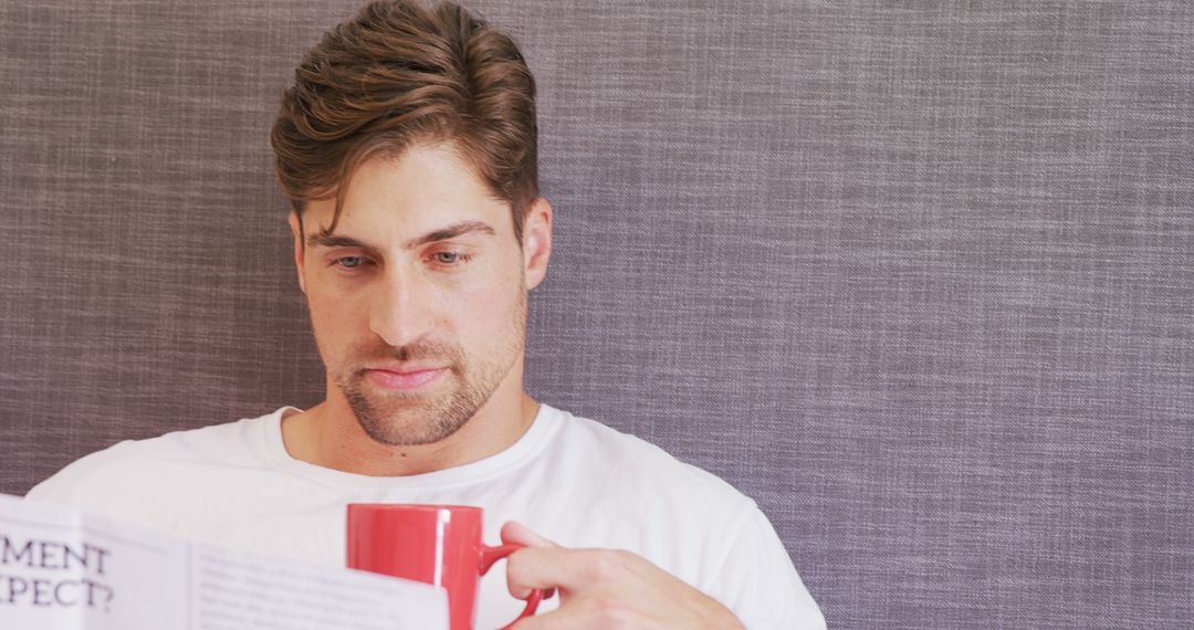 Man reading newspaper while holding red coffee cup - Free Images, Stock Photos and Pictures on Pikwizard.com