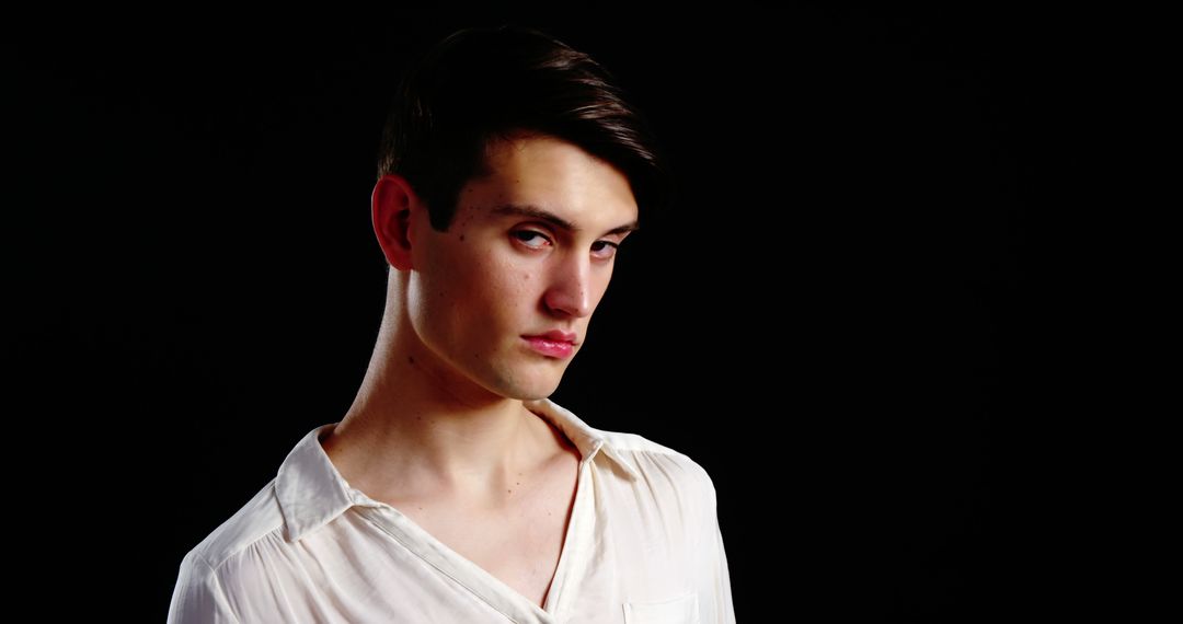 Young Man with Serious Expression in White Shirt Against Black Background - Free Images, Stock Photos and Pictures on Pikwizard.com