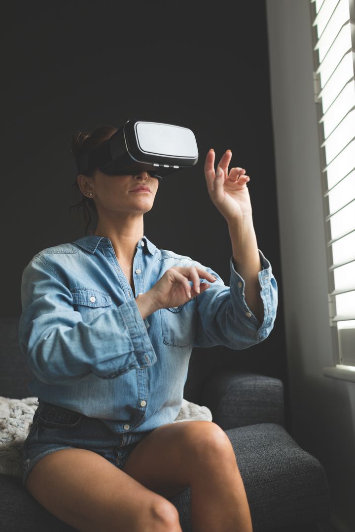 Woman using virtual reality headset while sitting on sofa in a comfortable home - Free Images, Stock Photos and Pictures on Pikwizard.com