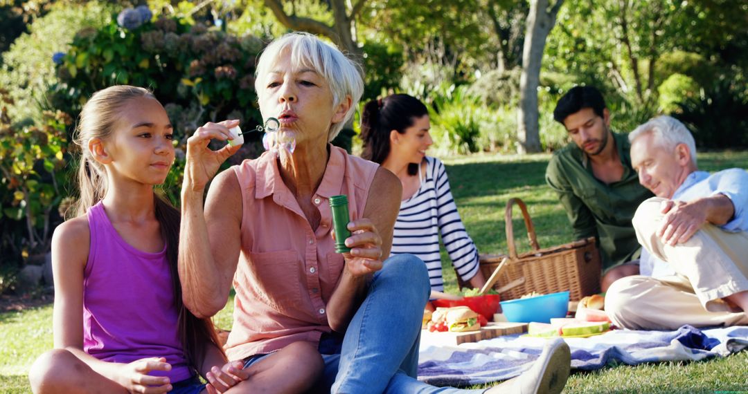 Grandmother Blowing Bubbles with Granddaughter at Family Picnic in Park - Free Images, Stock Photos and Pictures on Pikwizard.com