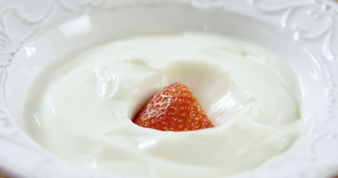 A fresh strawberry is partially submerged in creamy yogurt, with copy space - Free Images, Stock Photos and Pictures on Pikwizard.com