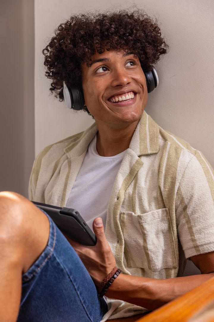 Young Man Listening to Music with Headphones While Relaxing with Tablet Indoors