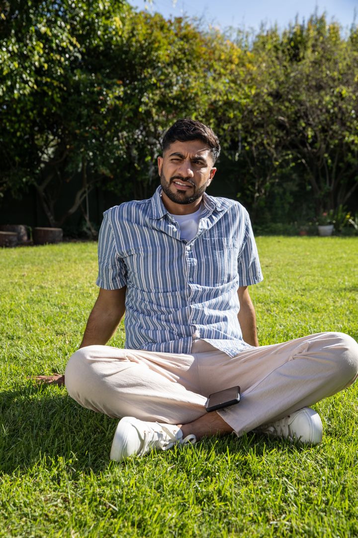 Man Relaxing Outdoors in Sunny Backyard Holding Smartphone