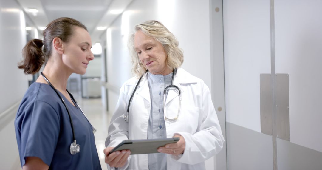 Two Female Doctors Reviewing Patient Information on Digital Tablet in Hospital Corridor - Free Images, Stock Photos and Pictures on Pikwizard.com