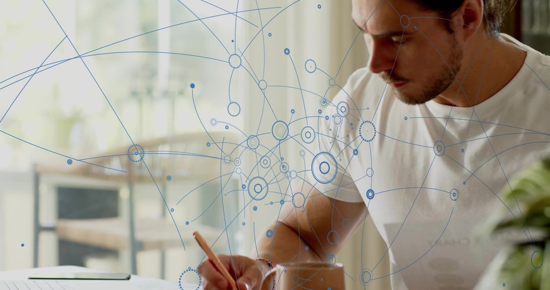 Young man writing at home desk with digital network overlay, remote work productivity