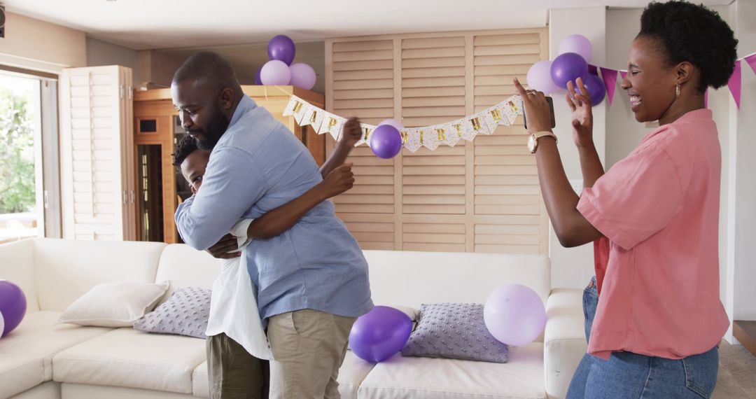 African American family celebrating with father hugging child while mother recording