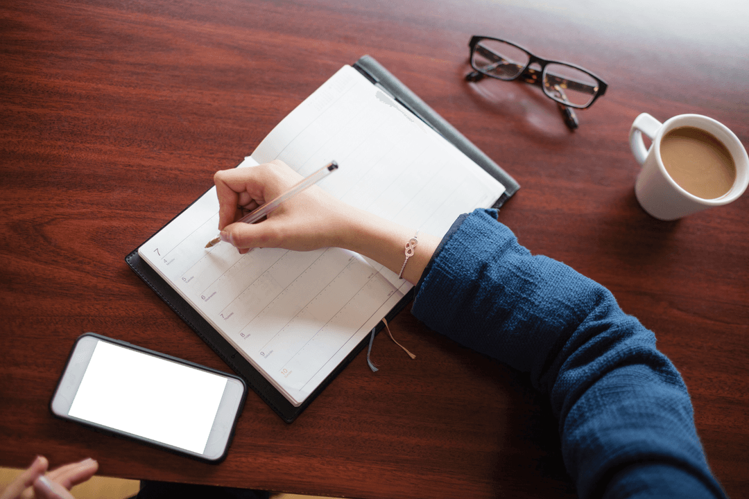 Transparent Hand Taking Notes in Planner on Wooden Desk