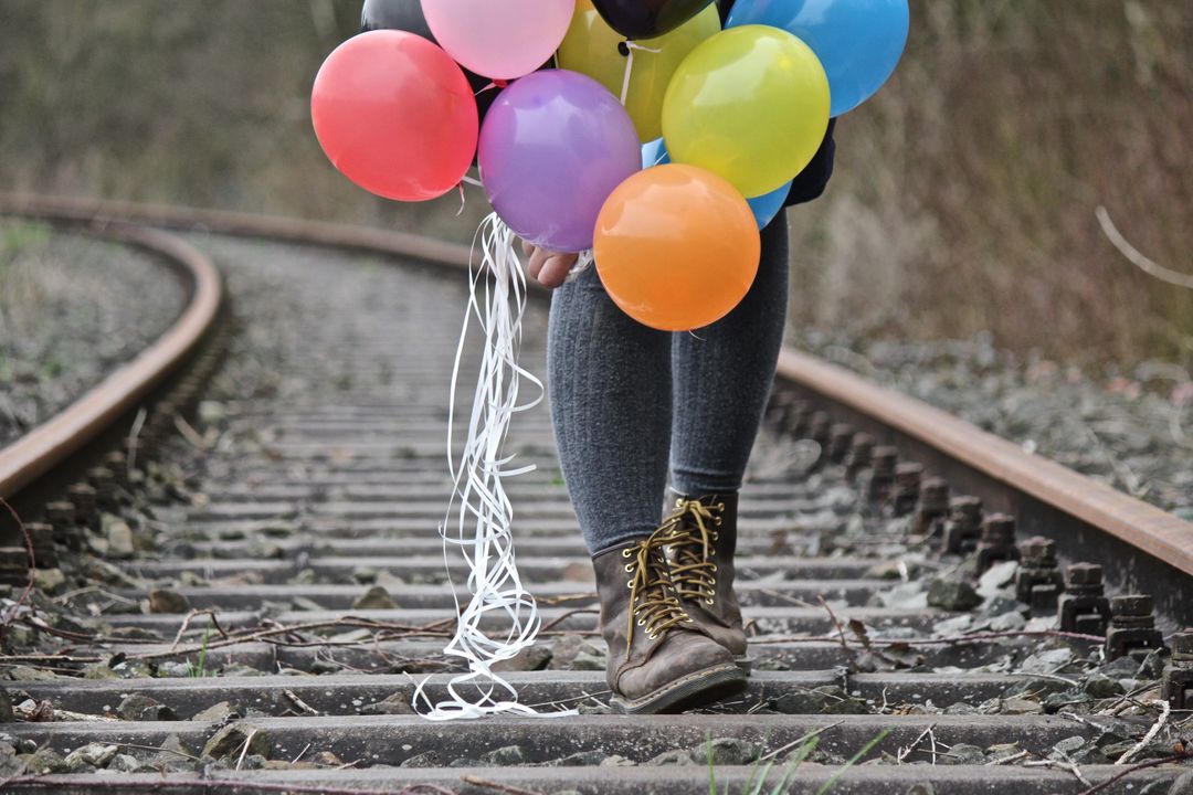 Person Holding Multicolored Balloons Walking Officially Railroad Tracks - Free Images, Stock Photos and Pictures on Pikwizard.com