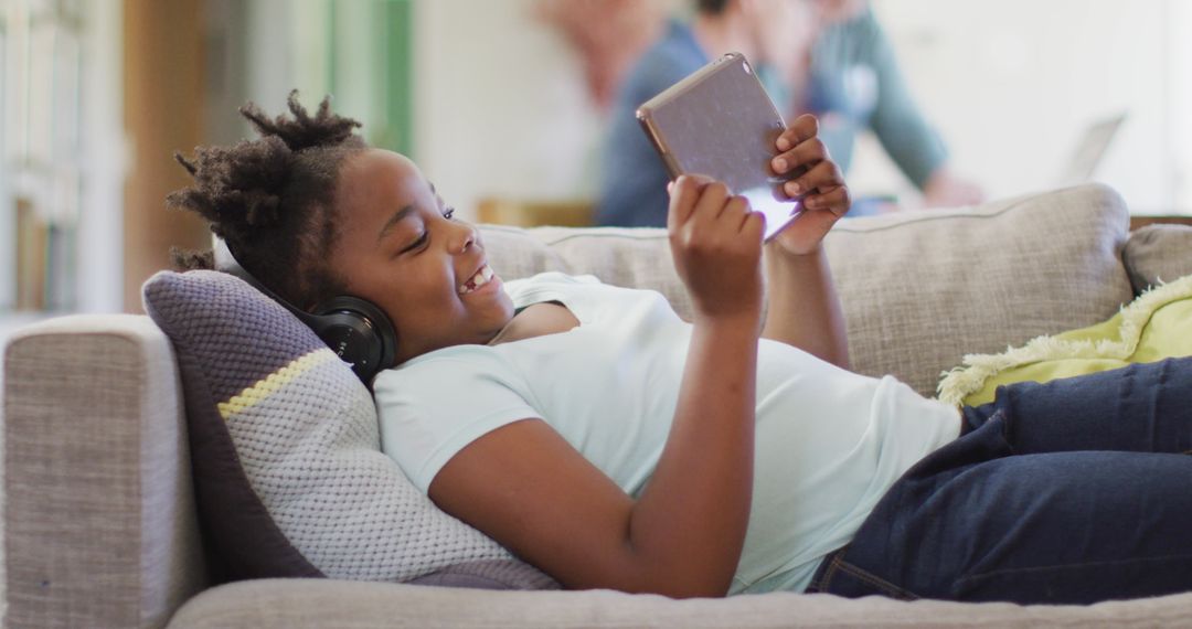 Joyful Girl with Headphones Using Tablet on Couch