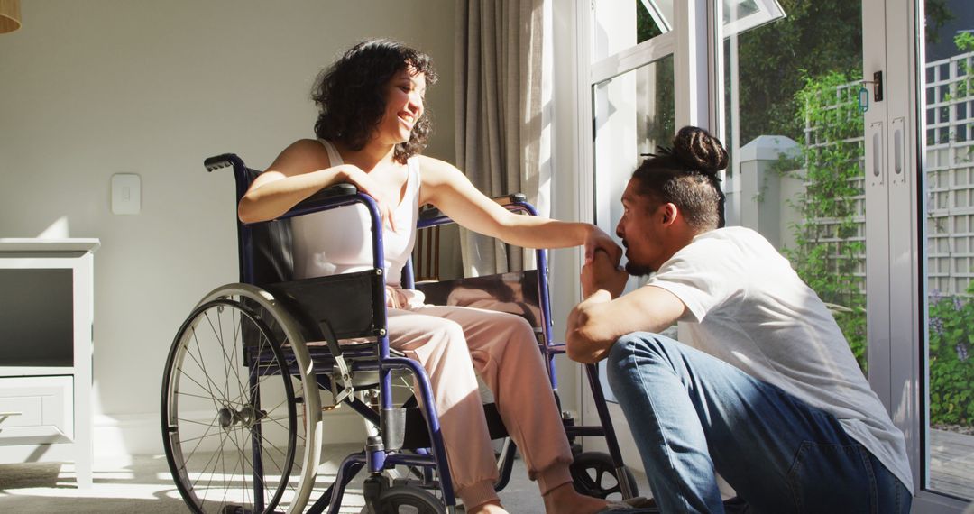 Happy biracial woman in wheelchair with smiling male partner kissing hand in sunny living room - Free Images, Stock Photos and Pictures on Pikwizard.com