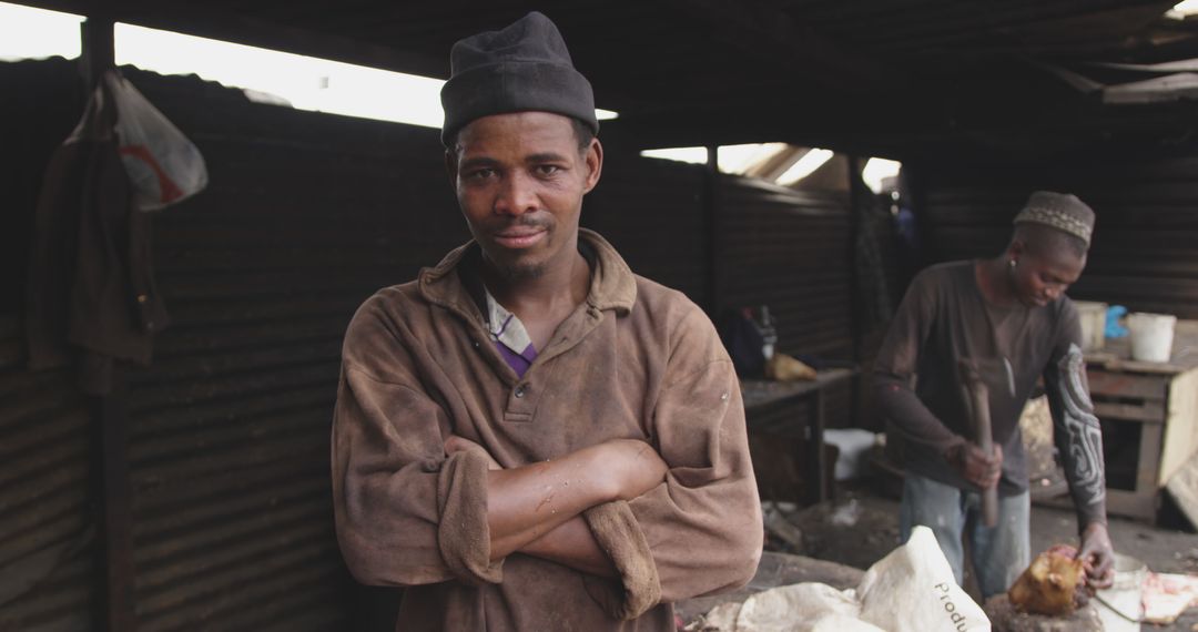 Serious African man standing in folded arms beside worker in informal workshop - Free Images, Stock Photos and Pictures on Pikwizard.com