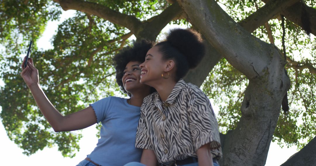 Two Young Women Taking Selfie Under Tree on Sunny Day - Free Images, Stock Photos and Pictures on Pikwizard.com