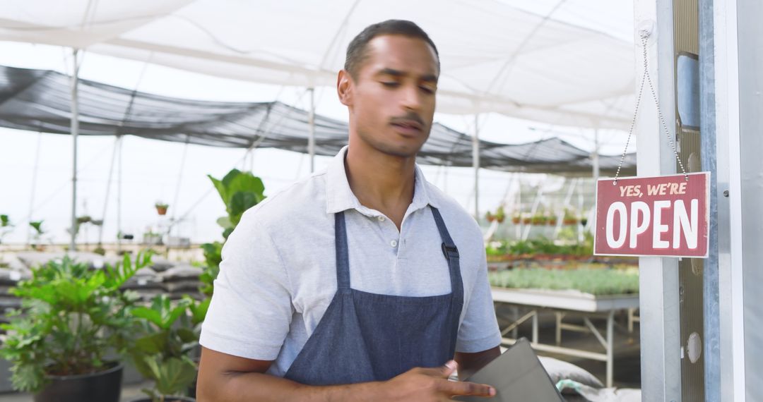 Greenhouse Worker Displaying Open Sign with Tablet and Plants