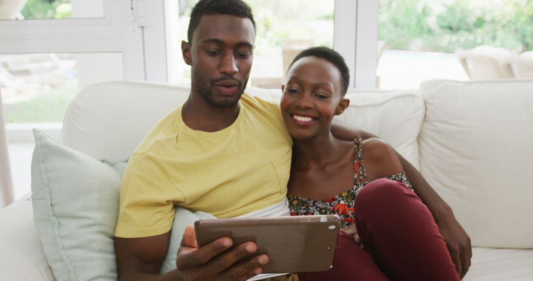 Happy african american couple sitting on sofa embracing and talking looking at tablet - Free Images, Stock Photos and Pictures on Pikwizard.com