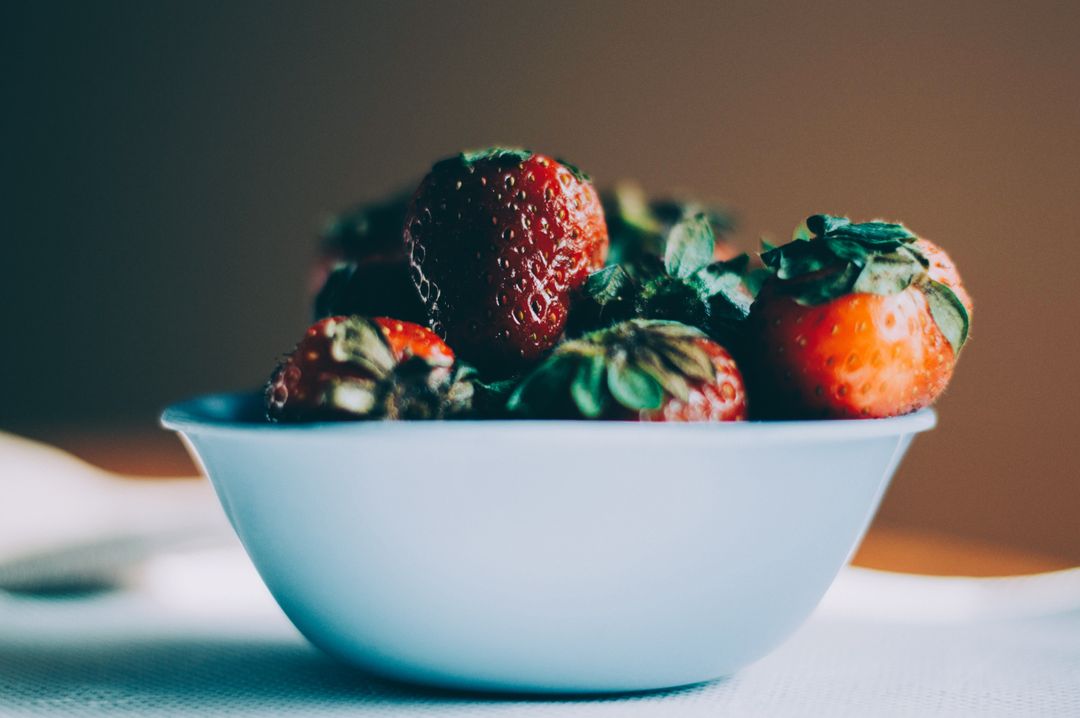 Fresh ripe strawberries overflowing in pale blue bowl with moody bokeh and soft light