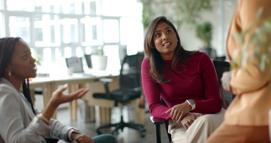Diverse female coworkers collaborating in modern open office, discussing ideas, smartwatch visible
