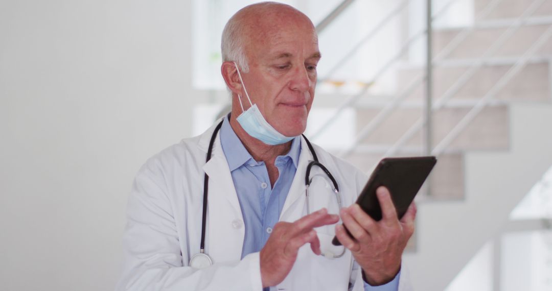 Senior Male Doctor Utilizing Tablet with Face Mask Around Neck - Free Images, Stock Photos and Pictures on Pikwizard.com