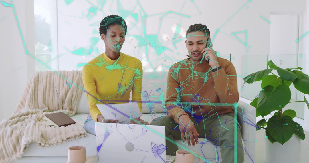 Collaborating duo reviewing documents and laptop on sunlit minimalist home sofa with phone