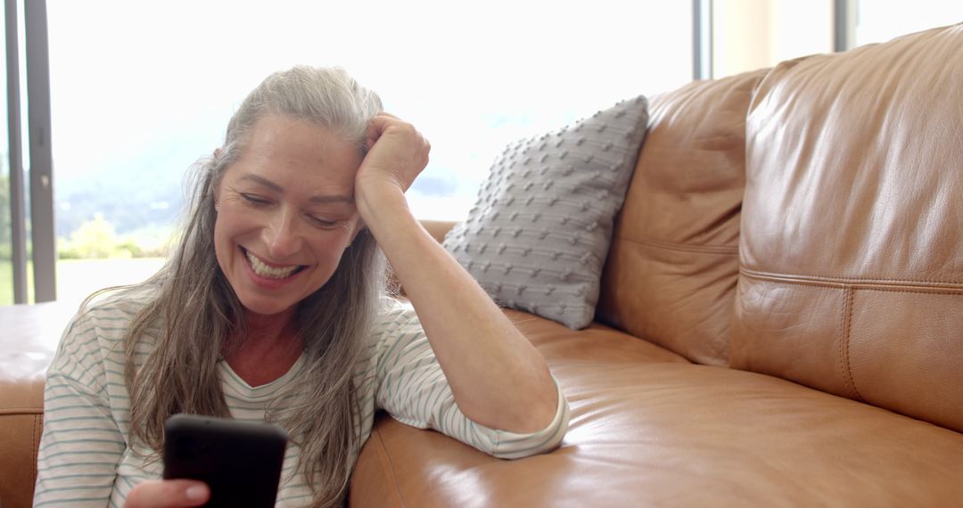 Happy Older Woman Relaxed on Couch Using Smartphone at Home