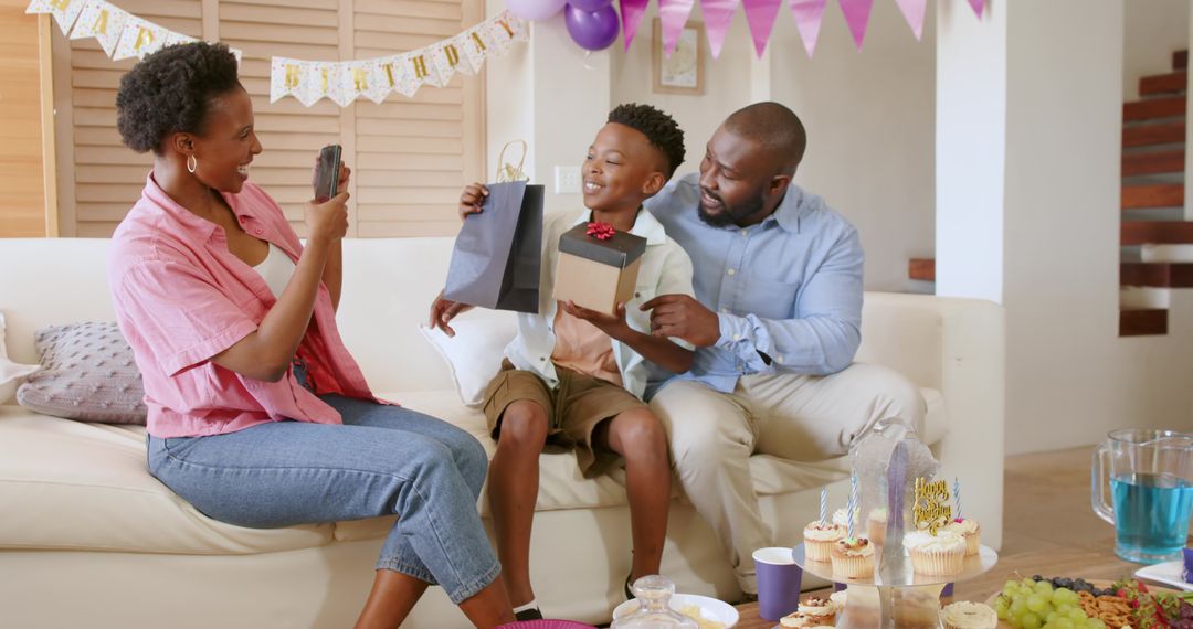 African American family celebrating birthday at home mom capturing moment dad handing gift