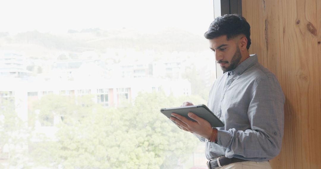 Man Using Tablet by Window in Modern Office Setting