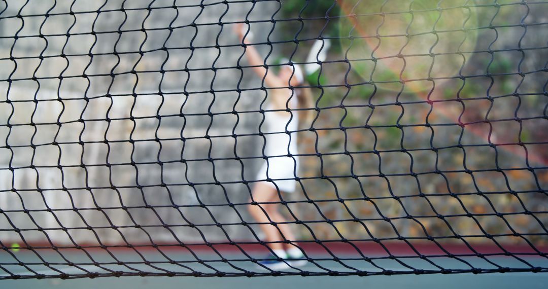 Blurred Tennis Player Serving Behind Net on Outdoor Court - Free Images, Stock Photos and Pictures on Pikwizard.com