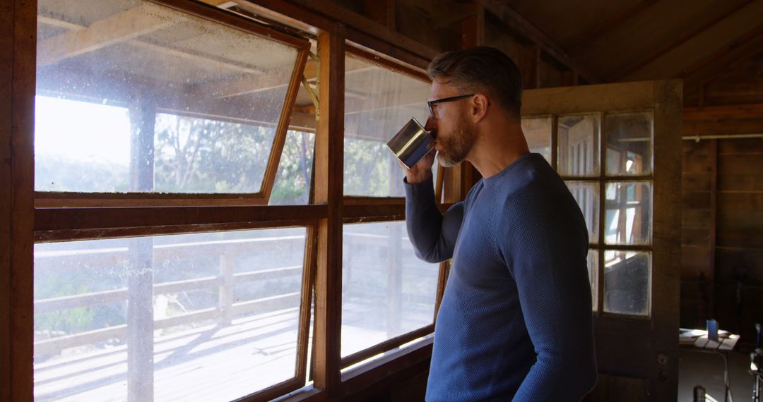 Man Drinking Coffee and Looking Out Cabin Window - Free Images, Stock Photos and Pictures on Pikwizard.com