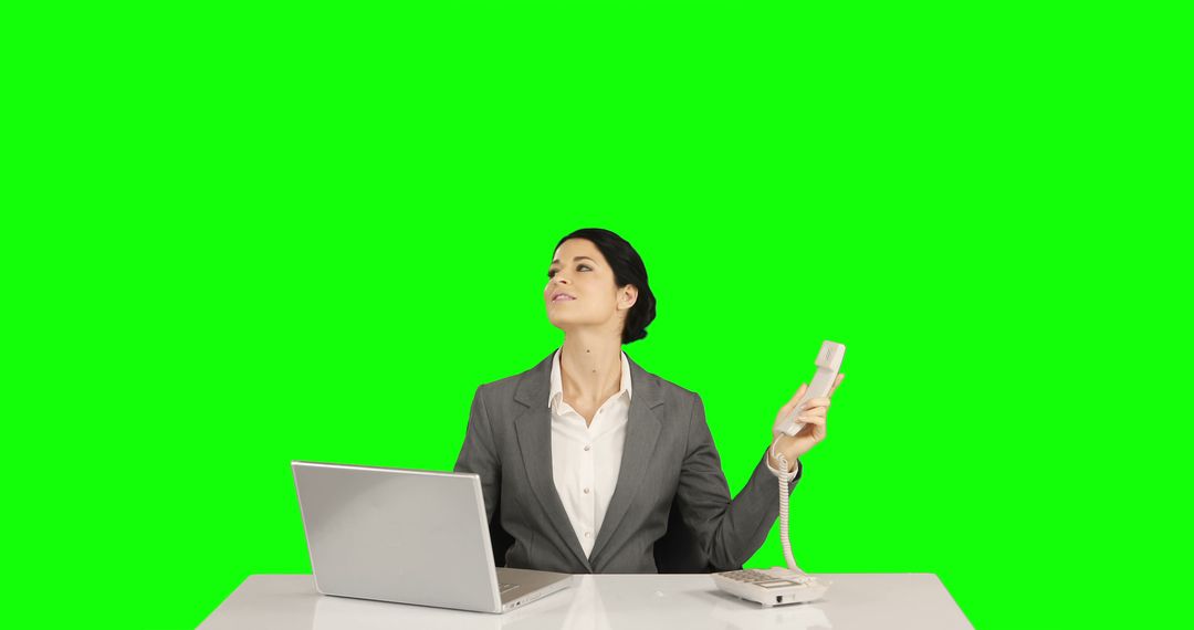 Businesswoman Holding Phone Receiver While Working on Laptop Against Green Screen - Free Images, Stock Photos and Pictures on Pikwizard.com