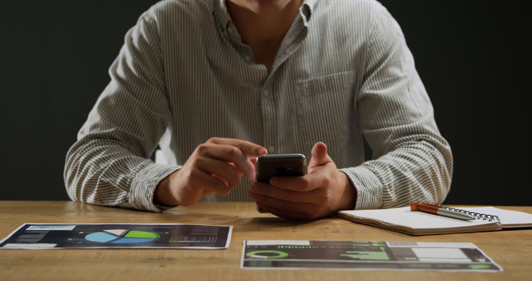 Businessman Using Smartphone at Desk with Financial Charts - Free Images, Stock Photos and Pictures on Pikwizard.com