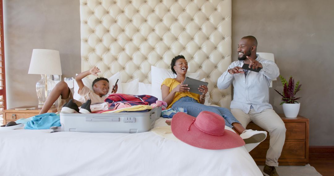 African American family unpacking suitcase on bed using tablet and smartphones smiling