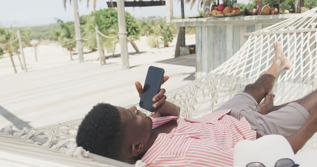 Young Man Relaxing in Hammock on Tropical Beach While Using Smartphone - Free Images, Stock Photos and Pictures on Pikwizard.com