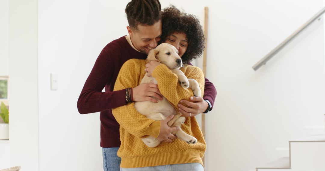 Multiracial couple cuddling light-colored puppy in cozy modern home