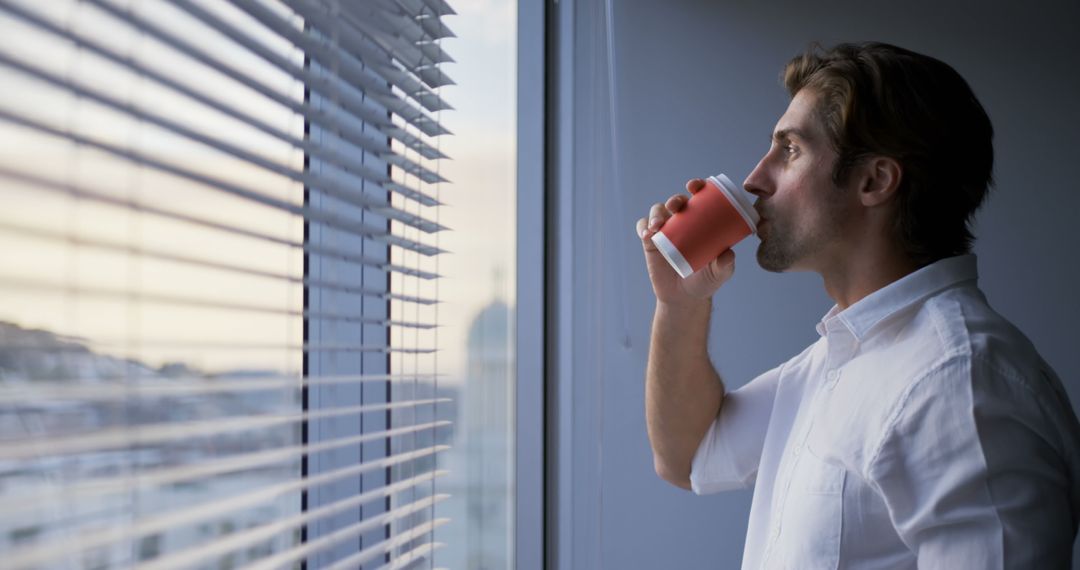 Young Executive Drinking Coffee While Looking Out Office Window