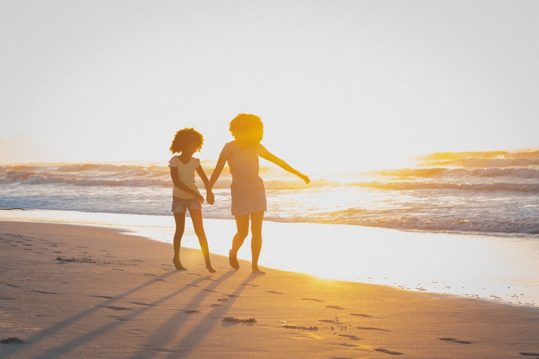 African American Mother and Daughter Walking on Beach at Sunset - Free Images, Stock Photos and Pictures on Pikwizard.com