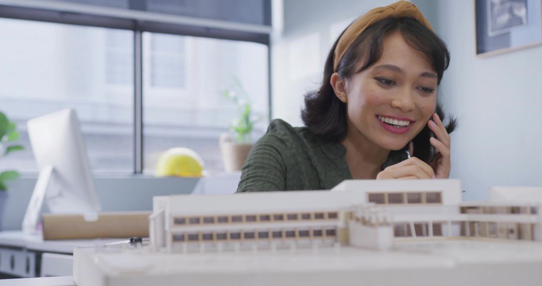 Asian architect woman on phone reviewing scale model in modern design studio