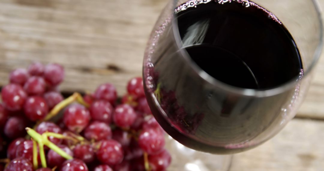 A glass of red wine is tilted on a wooden surface near a bunch of red grapes, with copy space - Free Images, Stock Photos and Pictures on Pikwizard.com