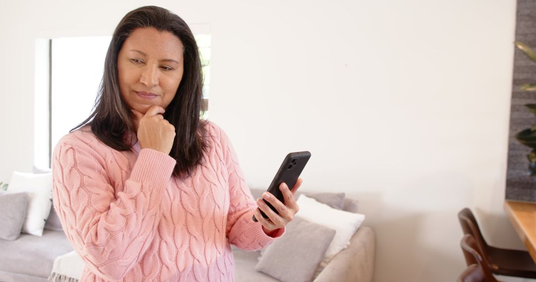 Woman Contemplating While Using Smartphone in Bright Living Room