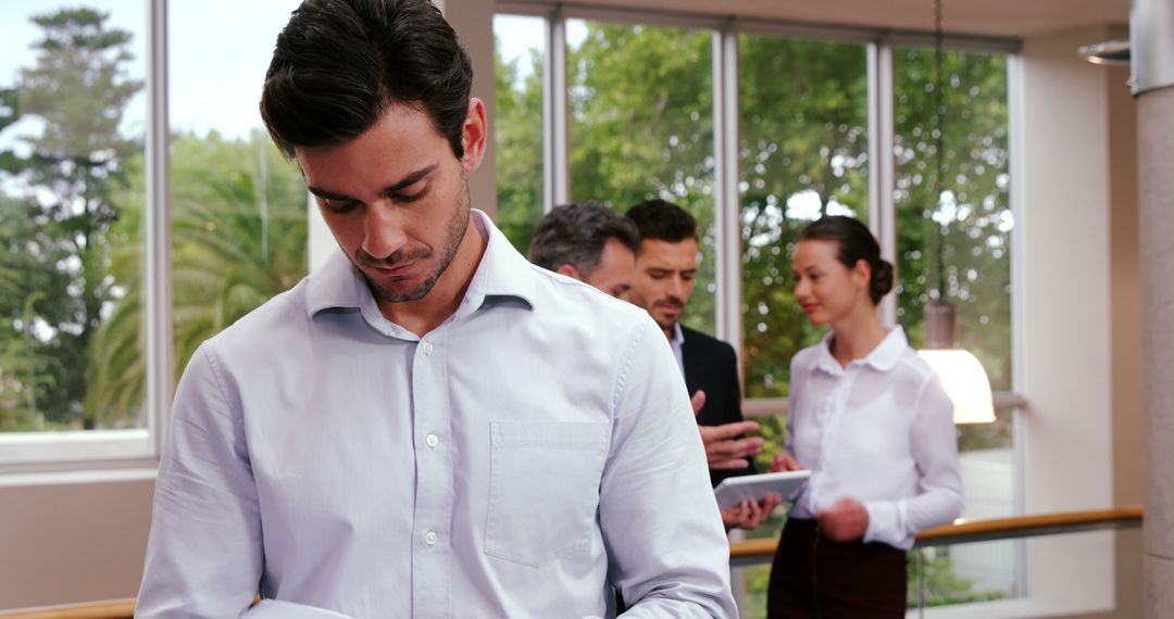 Focused Professional Man in Office Setting with Colleagues in Background