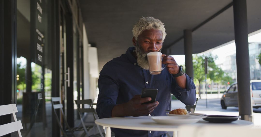 Businessman Enjoying Coffee While Checking Smartphone at Outdoor Cafe - Free Images, Stock Photos and Pictures on Pikwizard.com