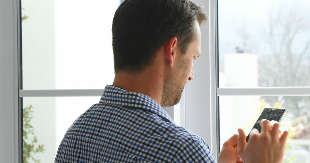 Man Using Smartphone by Window in Home Office - Free Images, Stock Photos and Pictures on Pikwizard.com