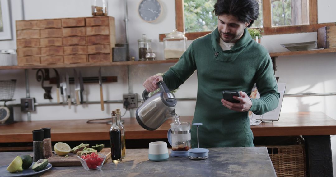 Man Preparing a Beverage in a Modern Kitchen while Using a Smartphone - Free Images, Stock Photos and Pictures on Pikwizard.com