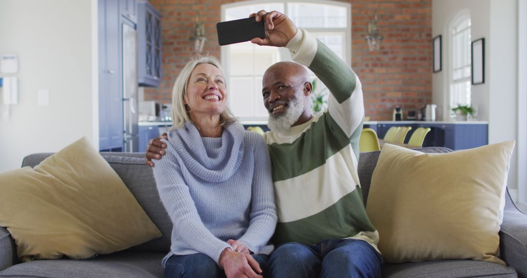 Happy senior diverse couple in living room sitting on sofa, using smartphone, making image call - Free Images, Stock Photos and Pictures on Pikwizard.com