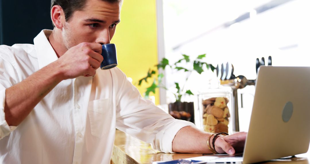 Focused Man Drinking Coffee While Using Laptop at Cafe