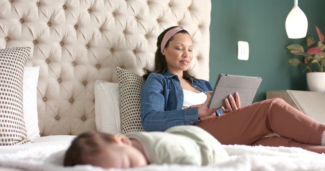 Relaxed Hispanic Mother Using Tablet While Infant Sleeps