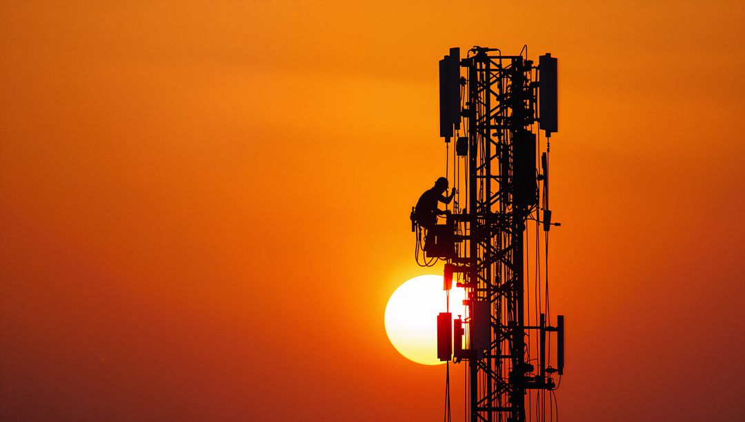 Silhouetted Telecom Technician Climbing Tower at Sunset
