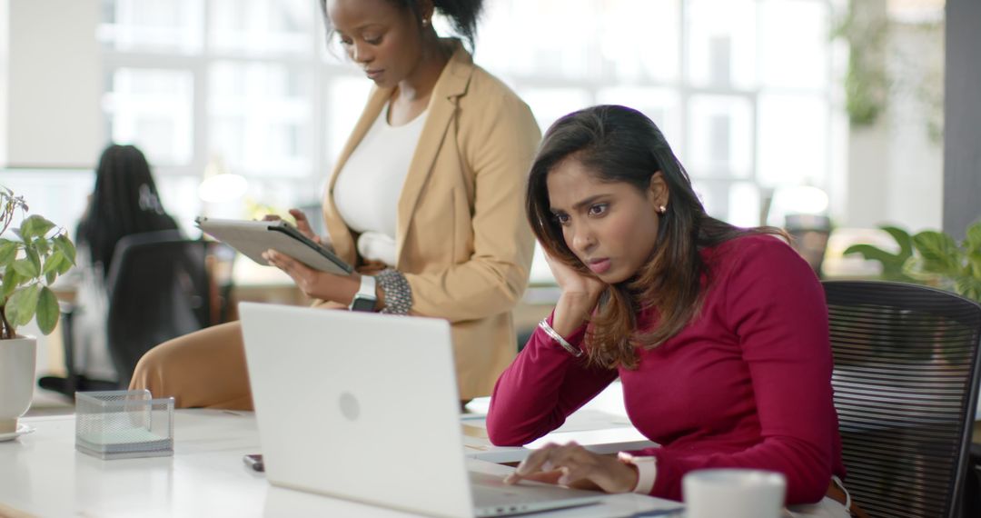 Black and South Asian Coworkers Collaborating on Laptop and Tablet in Modern Open Office