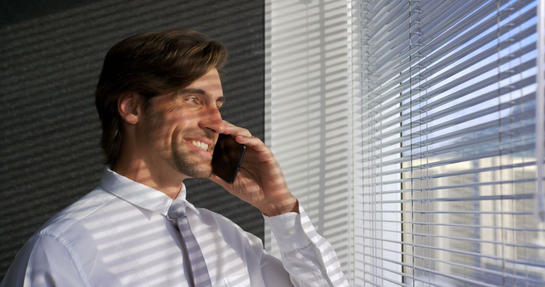Businessman Smiling While Talking on Mobile Phone by Office Window